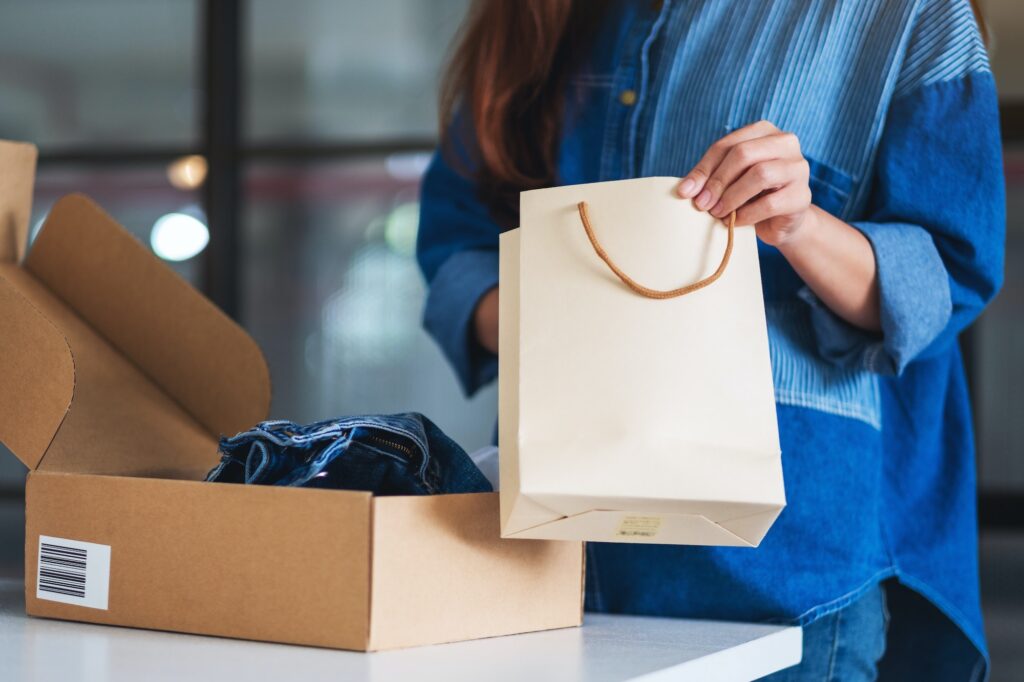 a woman opening a shopping bag with postal parcel box of clothing for delivery and online shopping